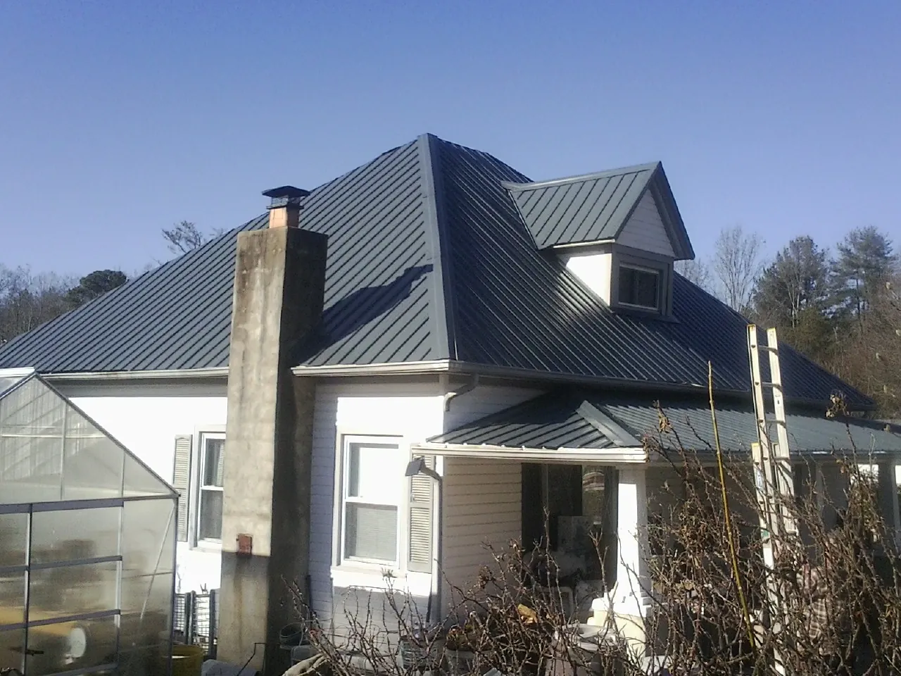 Dark blue standing seam metal roof on a white farmhouse with dormer — Slate & Tile Roof Repair by Roofing Brothers in Saint Hilaire