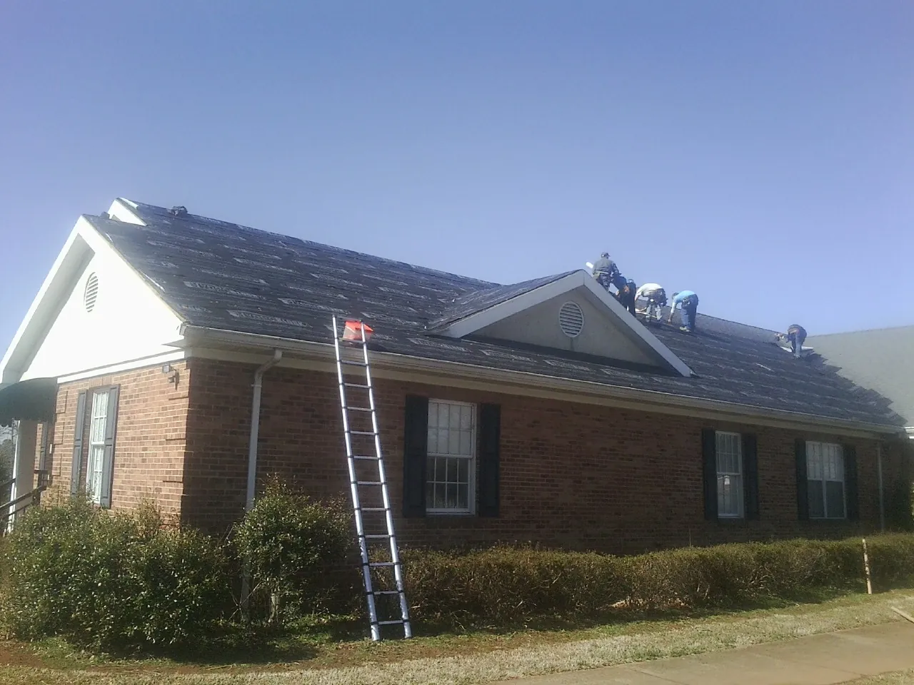 Crew tearing shingles off a brick ranch roof with a ladder set — Metal Roof Repair work by our crew in Saint Hilaire