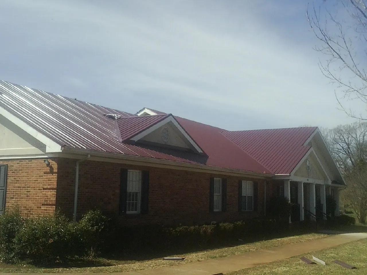 Red metal roof with gabled entries on a long brick building, from a Hail Damage Roof Repair job in Saint Hilaire