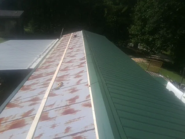 Old rusted panels beside newly installed green metal roofing — Wind Damage Roof Repair by Roofing Brothers in Saint Hilaire
