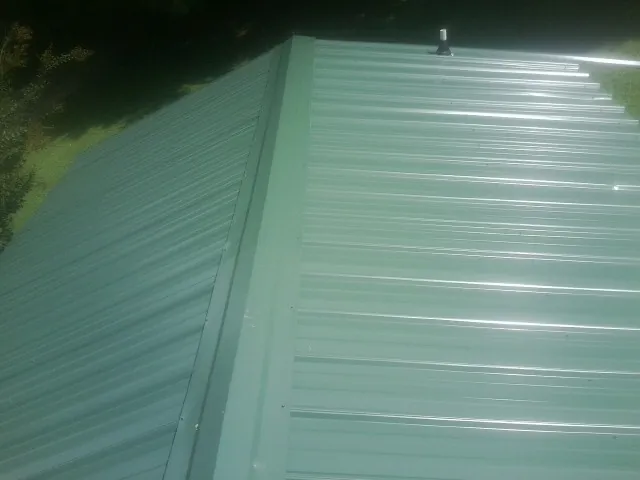 New green metal panels meeting at the ridge of a roof — Flat Roof Repair work by our crew in Saint Hilaire