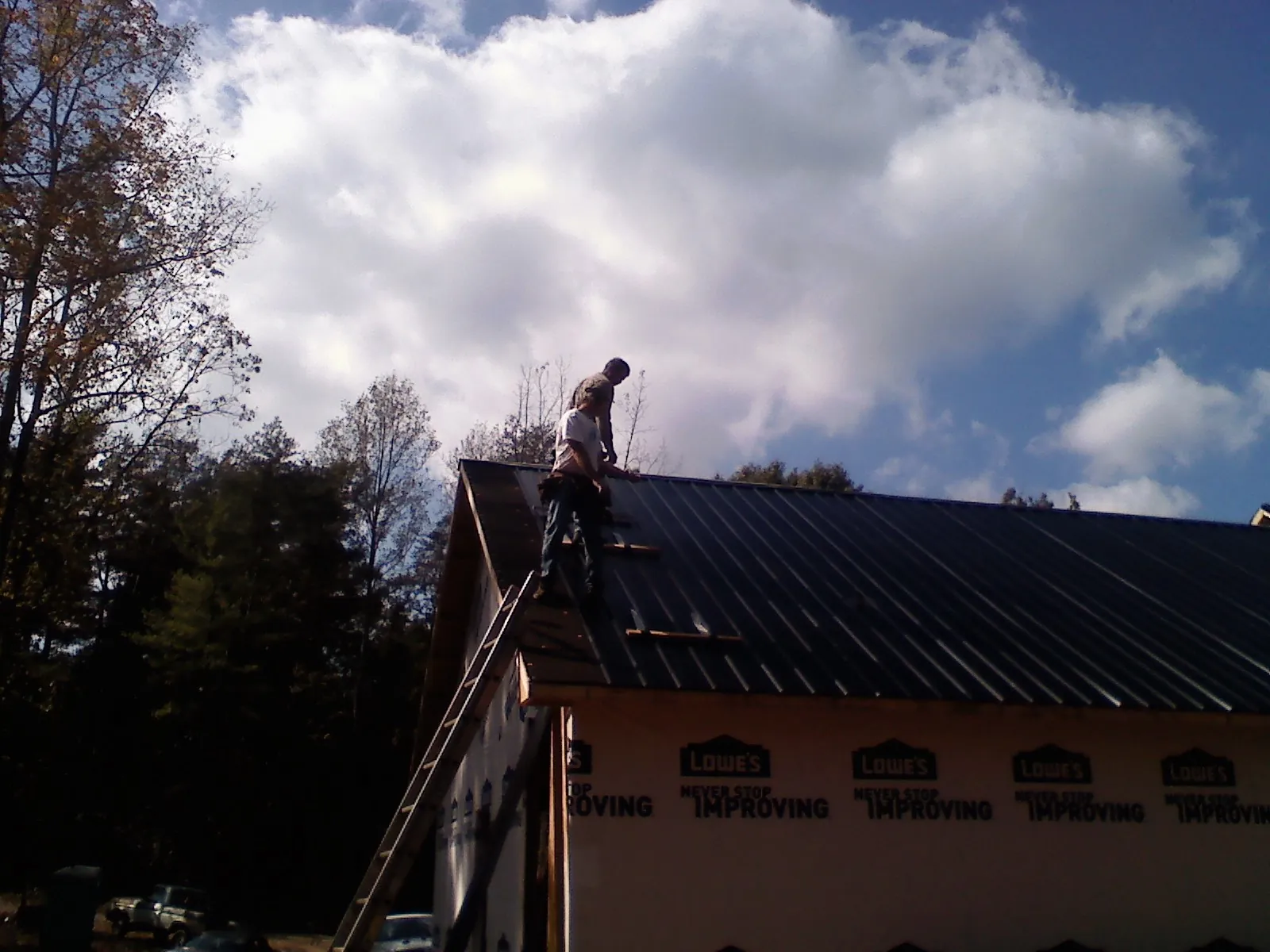 Roofer fastening dark metal panels high against a cloudy sky, from a Roof Inspection job in Saint Hilaire