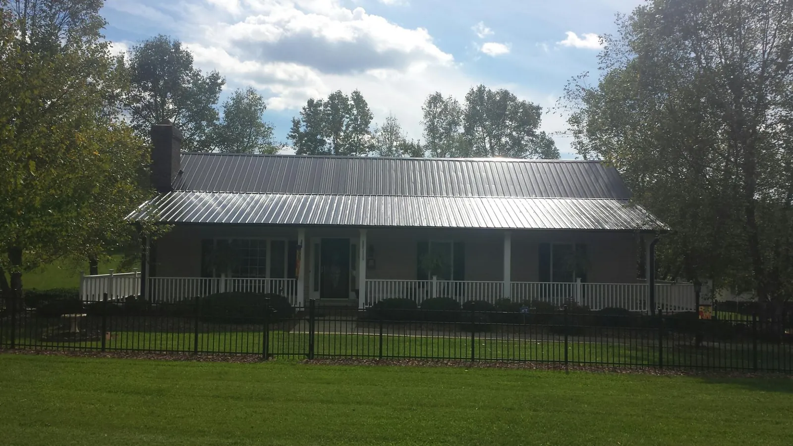 Gray metal roof on a brick ranch with a full width front porch — Gutter Guard Installation work by our crew in Saint Hilaire