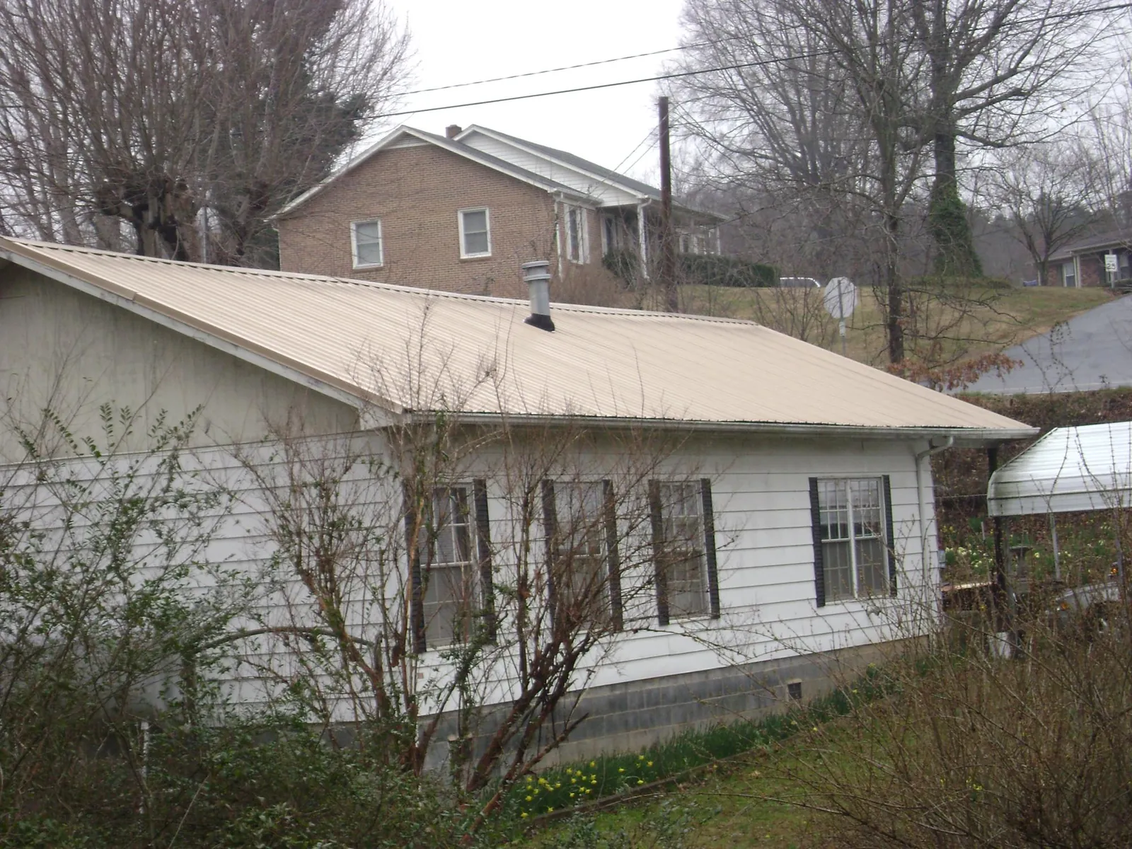 Tan metal roof on a white sided house set into a hillside — Commercial Roofing by Roofing Brothers in Saint Hilaire