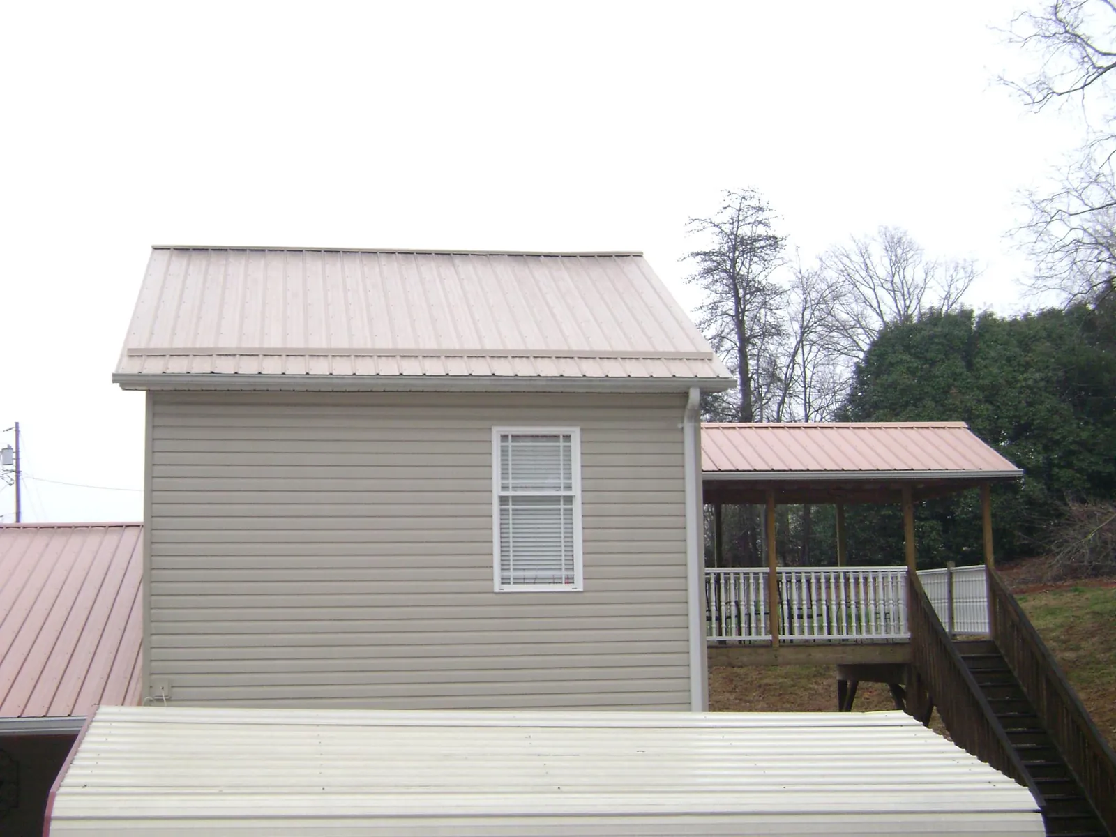 Tan metal roofs on a two story addition and attached porch, from a Roof Replacement job in Saint Hilaire